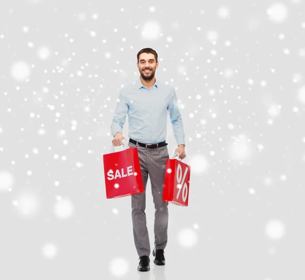 Uśmiechnięty mężczyzna z czerwonych torby na zakupy na śniegu — Zdjęcie stockowe