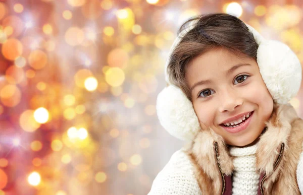 Happy little girl in earmuffs over holidays lights — Stock Photo, Image