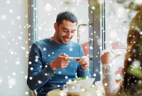Glückliches Paar beim Essen mit dem Smartphone im Café — Stockfoto
