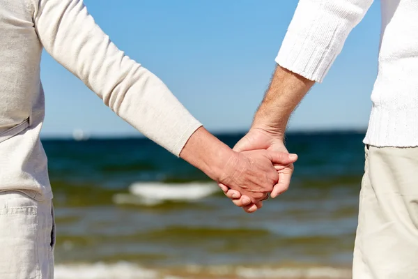Close up of senior couple holding hands on beach — Stock Photo, Image