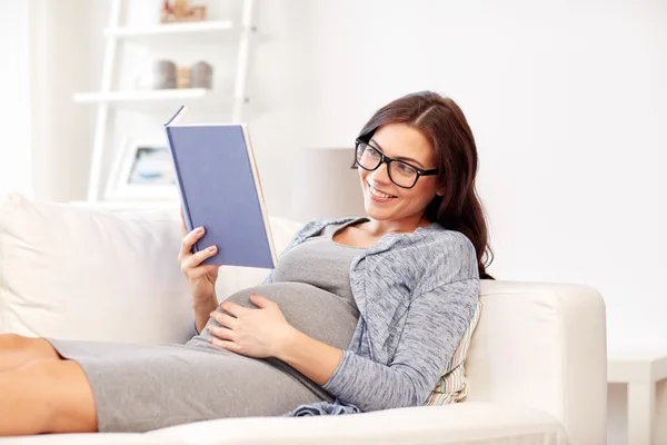 Счастливая беременная женщина читает книгу дома — стоковое фото