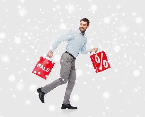 Hombre sonriente con bolsas de compras rojas sobre nieve — Foto de Stock