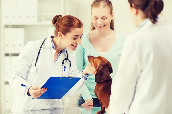 Happy woman with dog and doctor at vet clinic — Stock Photo, Image