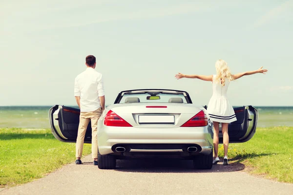 Happy man and woman near cabriolet car at sea — Stock Photo, Image