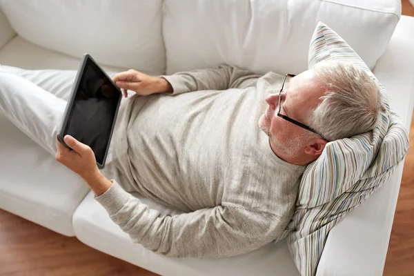 Homem sênior com tablet pc deitado no sofá em casa — Fotografia de Stock