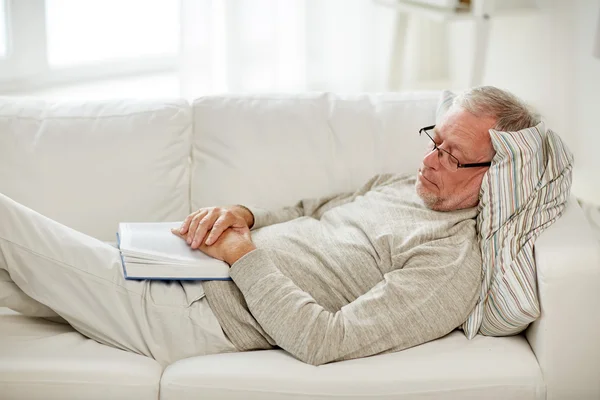 Старший мужчина спит на диване с книгой дома — стоковое фото
