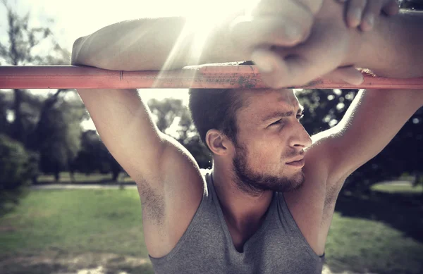 Joven ejercitándose en barra horizontal al aire libre —  Fotos de Stock