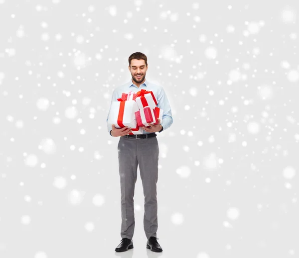 Щасливий молодий чоловік тримає різдвяні подарунки над снігом — стокове фото