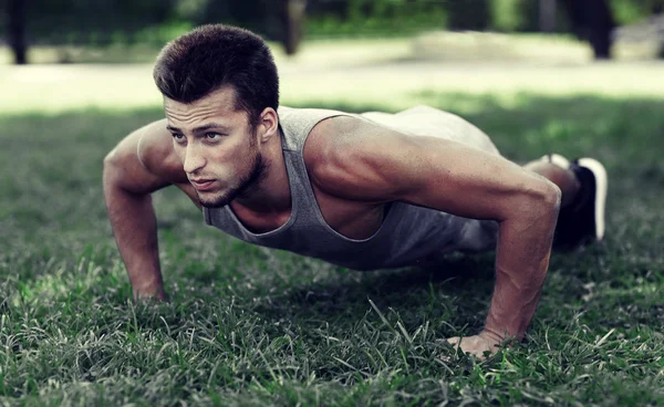 Jonge man doet push ups op gras in zomer park — Stockfoto