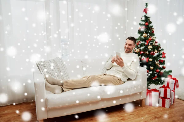 Glimlachende man met smartphone thuis voor Kerstmis — Stockfoto