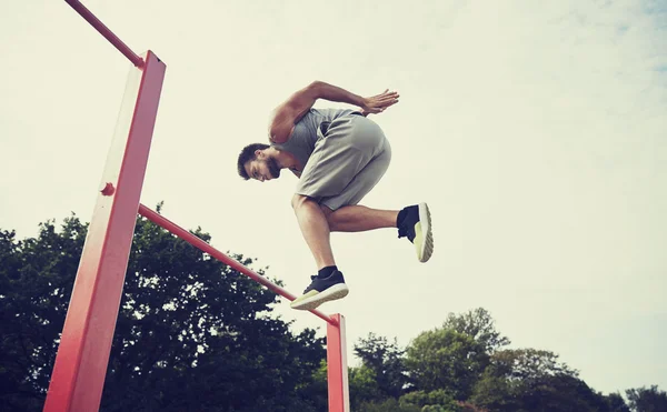 Jonge man springen op horizontale balk buitenshuis — Stockfoto