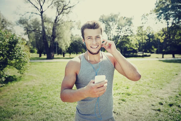 Gelukkig man met oortelefoons en smartphone bij park — Stockfoto