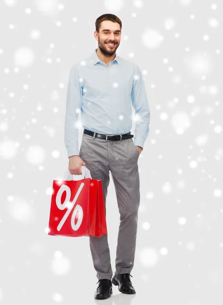 Uomo sorridente con shopping bag rossa sopra la neve — Foto Stock