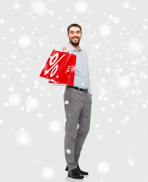 Uomo sorridente con shopping bag rossa sopra la neve — Foto Stock