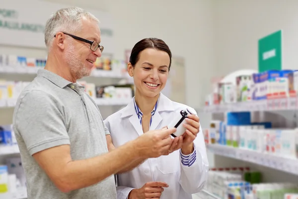 Фармацевт показывает лекарство старшему мужчине в аптеке — стоковое фото