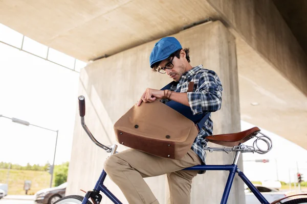 Hipster homem com bicicleta procurando algo no saco — Fotografia de Stock