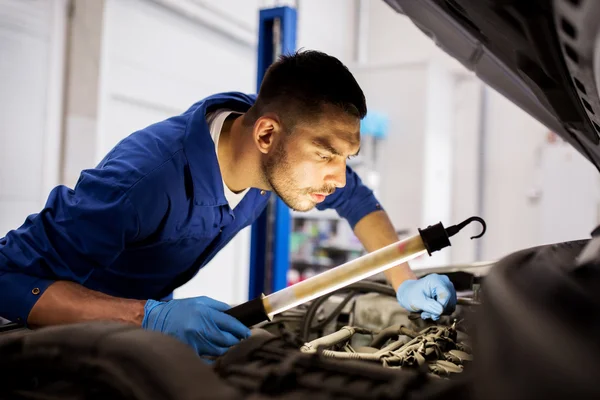 Mecânico homem com lâmpada reparando carro na oficina — Fotografia de Stock