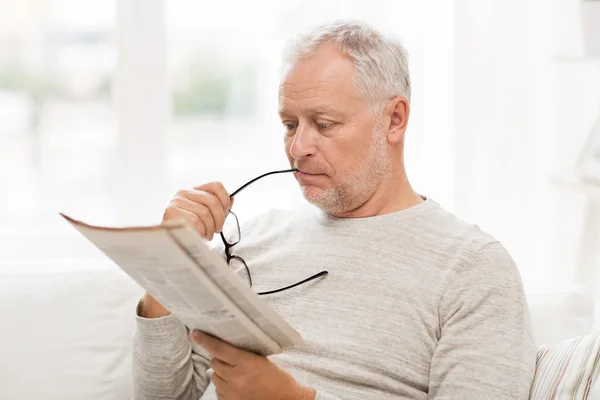 Äldre mannen i glasögon läsa tidningen hemma — Stockfoto