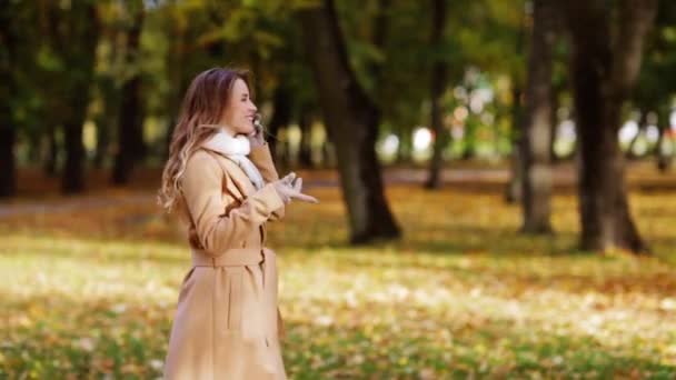 Woman with smartphone walking in autumn park — ストック動画
