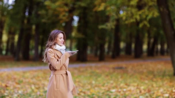 Woman with smartphone walking in autumn park — Stockvideo