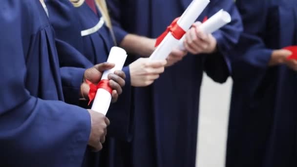 Estudantes em vestidos de solteiro segurando pergaminhos diploma — Vídeo de Stock