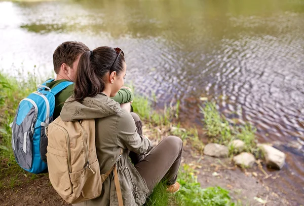 Coppia con zaini seduti sulla riva del fiume — Foto Stock