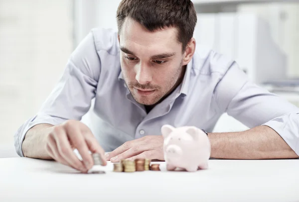 Hombre de negocios con alcancía y monedas en la oficina —  Fotos de Stock