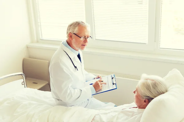 Senior woman and doctor with clipboard at hospital — Stock Photo, Image