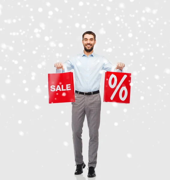 Hombre sonriente con bolsas de compras rojas sobre nieve —  Fotos de Stock