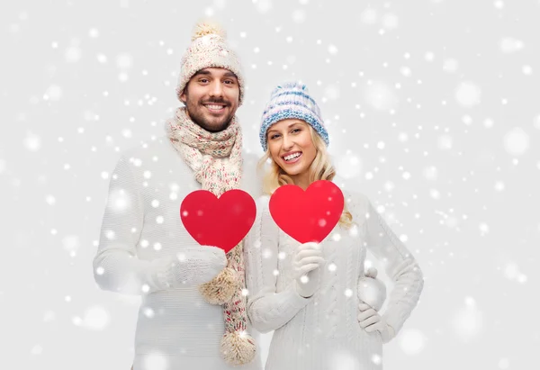 Casal sorridente em roupas de inverno com corações vermelhos — Fotografia de Stock