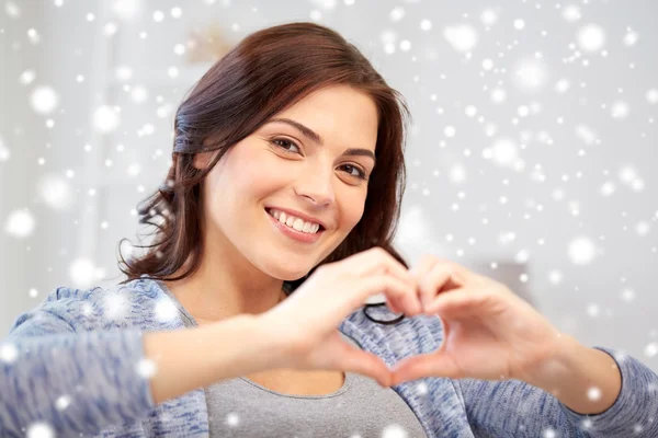 Happy young woman showing heart with hands at home — Stockfoto