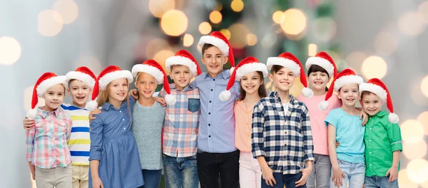 Glücklich lächelnde Kinder in Weihnachtsmützen, die sich umarmen — Stockfoto