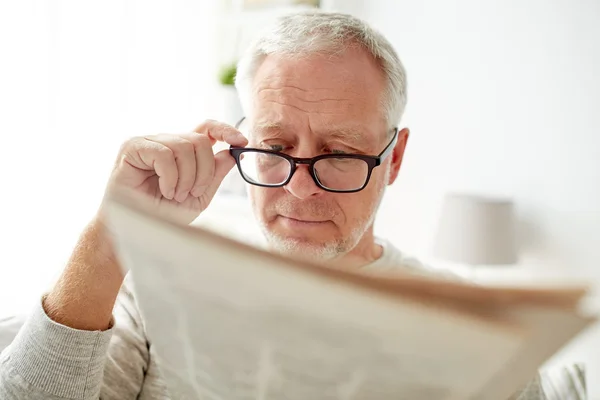 Senior man in glasses reading newspaper at home — Stock Photo, Image