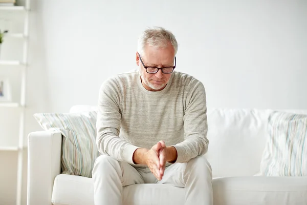 Senior man sitting on sofa at home and thinking — Stock Photo, Image