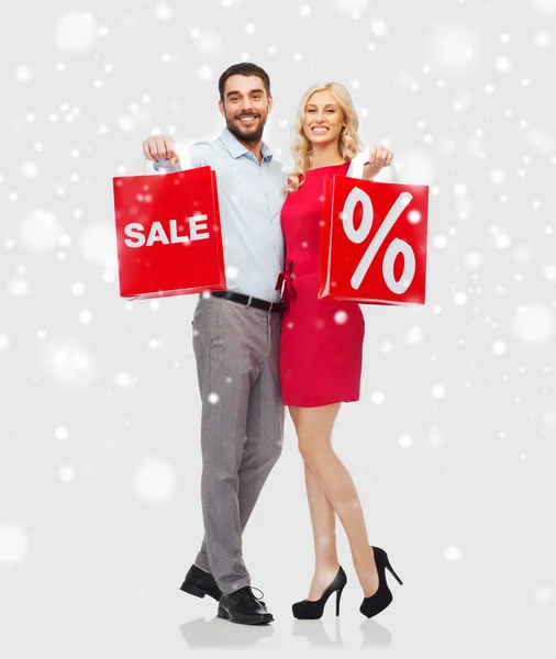 Casal feliz com sacos de compras vermelhas sobre a neve — Fotografia de Stock