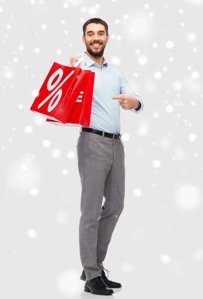 Uomo sorridente con borse della spesa rosse sulla neve — Foto Stock