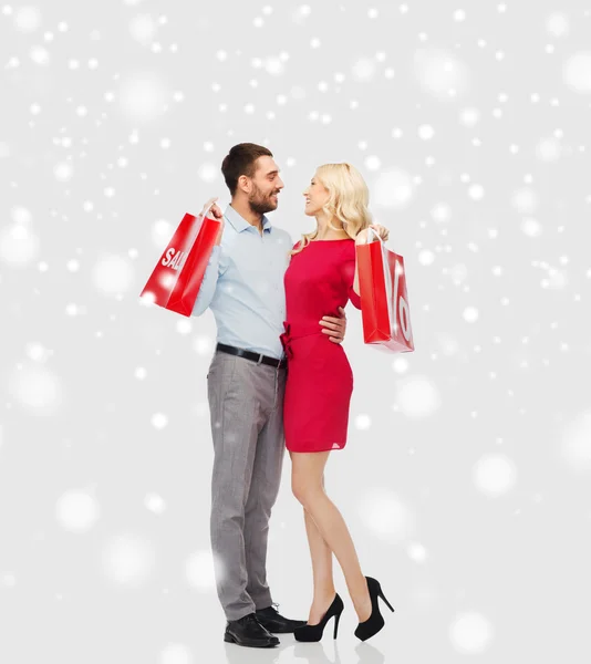 Счастливая пара с красными мешками для покупок на снегу — стоковое фото