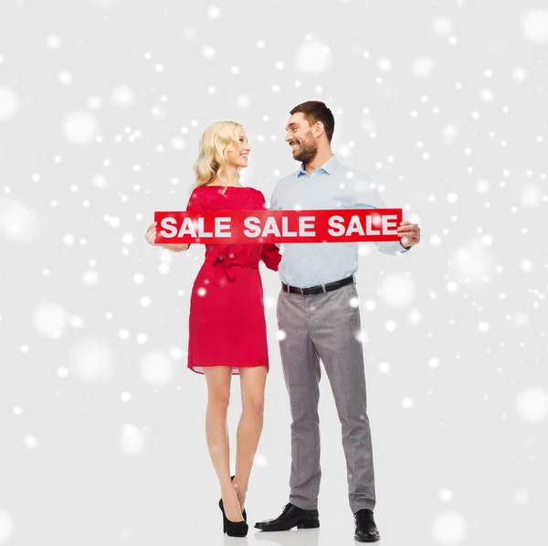 Happy couple with red sale sign over snow — Stock Photo, Image