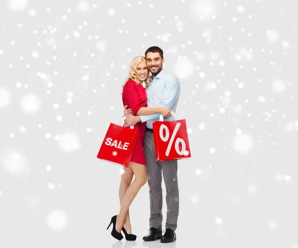 Casal feliz com sacos de compras vermelhas sobre a neve — Fotografia de Stock