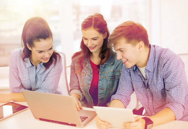 Три улыбающихся студента с ноутбуком и планшетным компьютером — стоковое фото