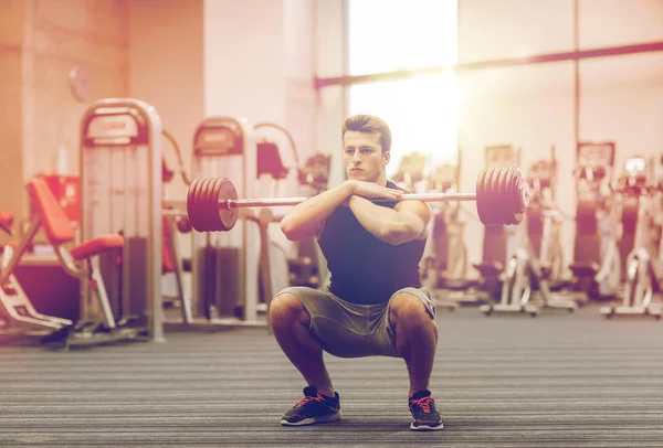 Jovem homem flexionando músculos com barbell no ginásio — Fotografia de Stock