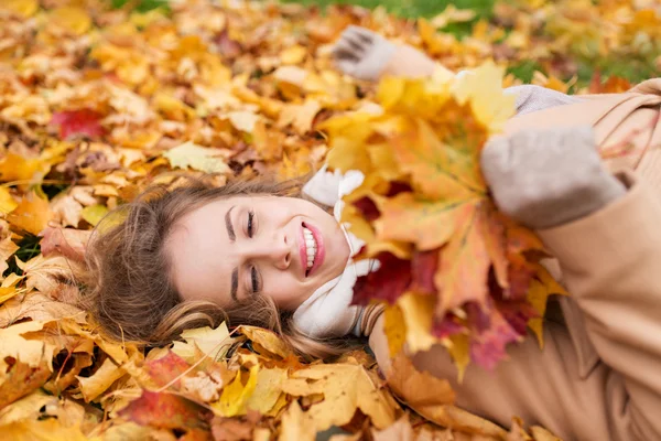 Schöne glückliche Frau, die auf Herbstblättern liegt — Stockfoto