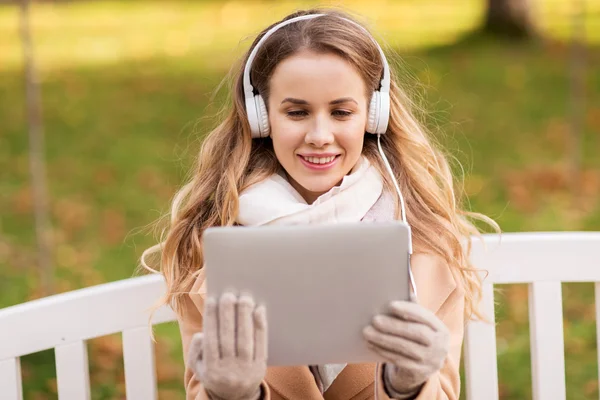 Mujer con tablet PC y auriculares en el parque de otoño — Foto de Stock