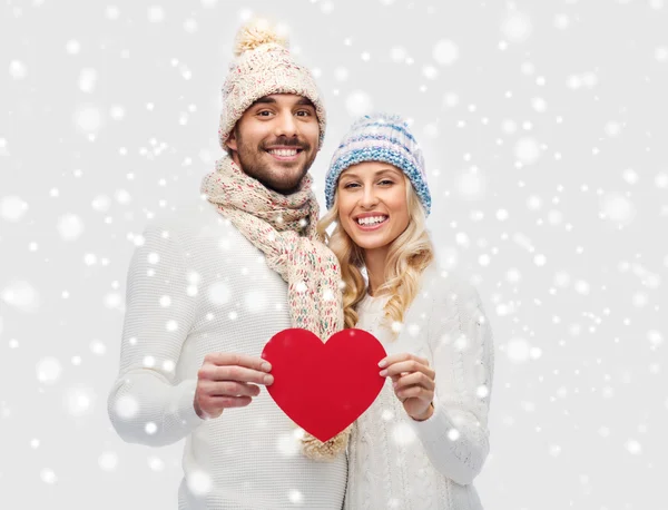 Casal sorridente em roupas de inverno com coração vermelho — Fotografia de Stock