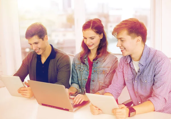 Tre leende studenter med bärbara datorer och tablet pc — Stockfoto