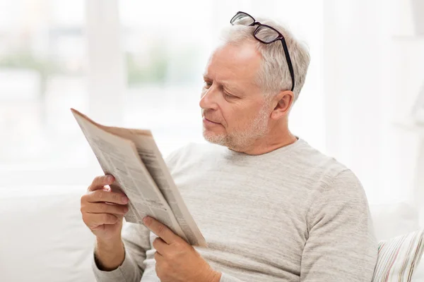 Äldre mannen i glasögon läsa tidningen hemma — Stockfoto