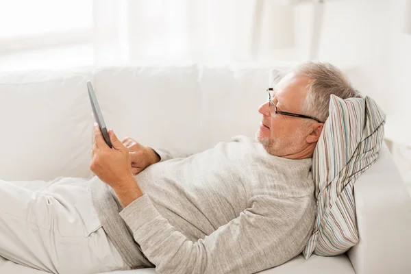 Uomo anziano con tablet pc sdraiato sul divano di casa — Foto Stock