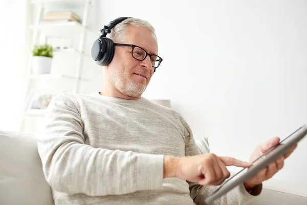 Homem idoso com tablet pc e fones de ouvido em casa — Fotografia de Stock