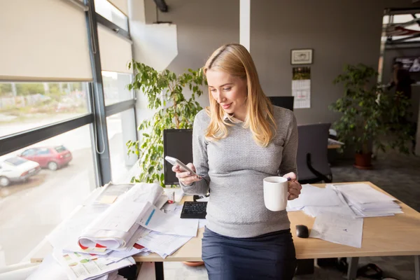 Mujer de negocios embarazada con teléfono inteligente en la oficina — Foto de Stock