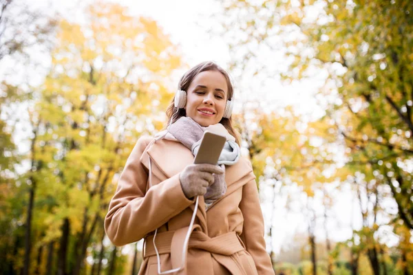Kvinna med smartphone och hörlurar i höst park — Stockfoto